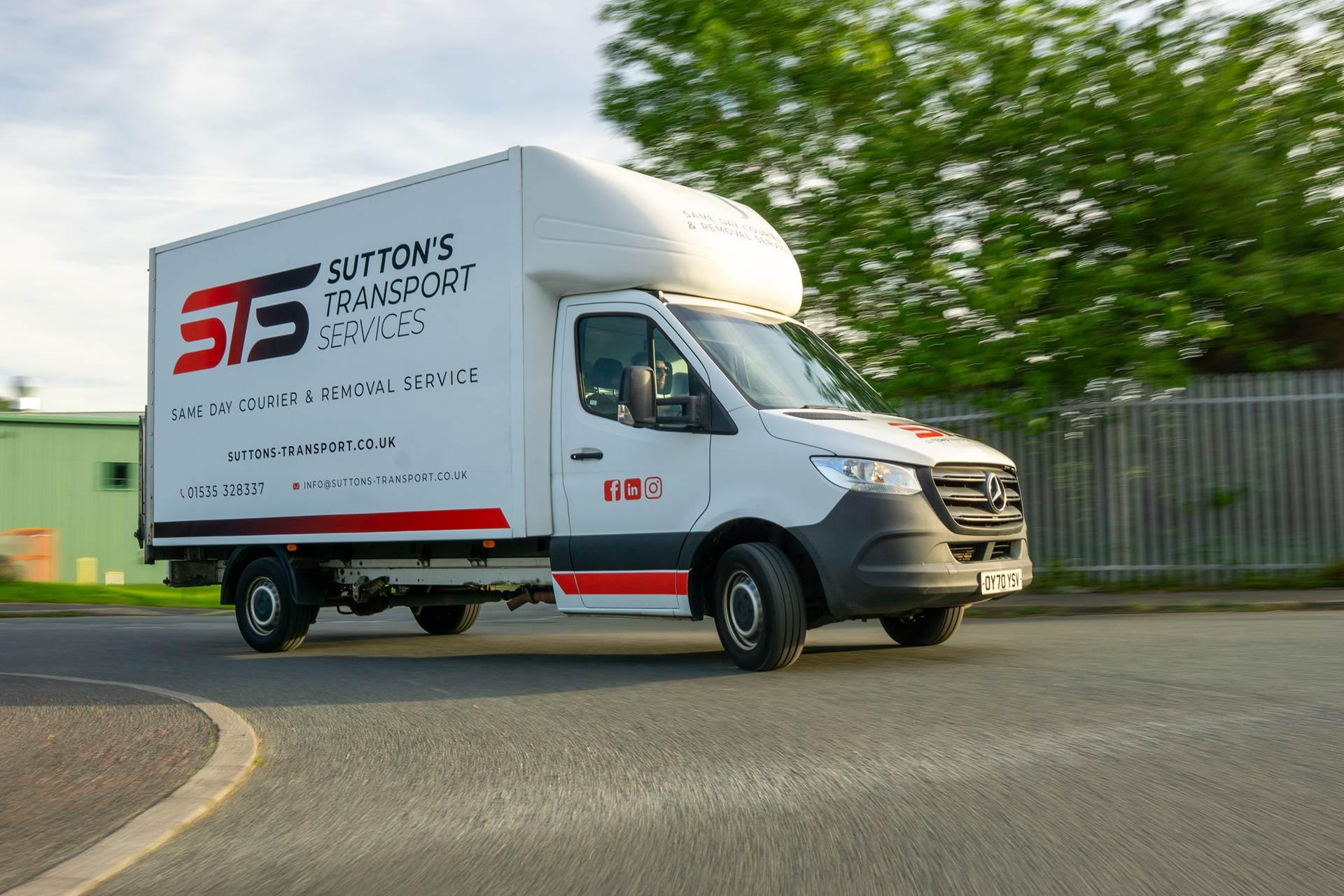Branded luton van driving around a bend from the side